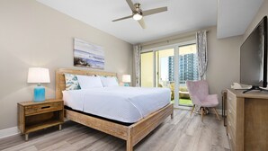 A hotel room with a bed, a desk, a chair, a TV, and a balcony with a view of buildings. - Ariel Dunes I 303 * Last minute savings. Walk to Beach! Salt Water Vacations (Destin)