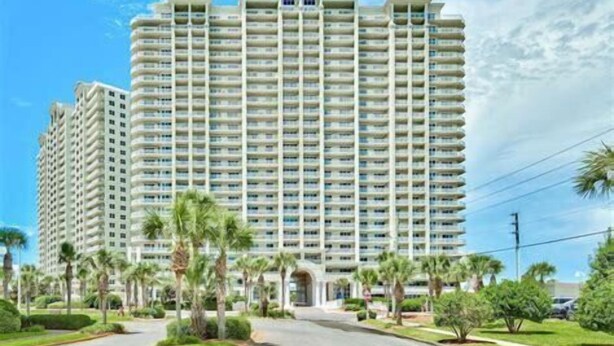 A high-rise hotel with multiple balconies, a central entrance, and a well-maintained surrounding with palm trees and greenery. - Ariel Dunes I 303 * Last minute savings. Walk to Beach! Salt Water Vacations (Destin)