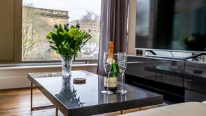 Un salon moderne avec une table en verre, un vase contenant des plantes vertes, une bouteille de champagne et deux coupes à champagne.