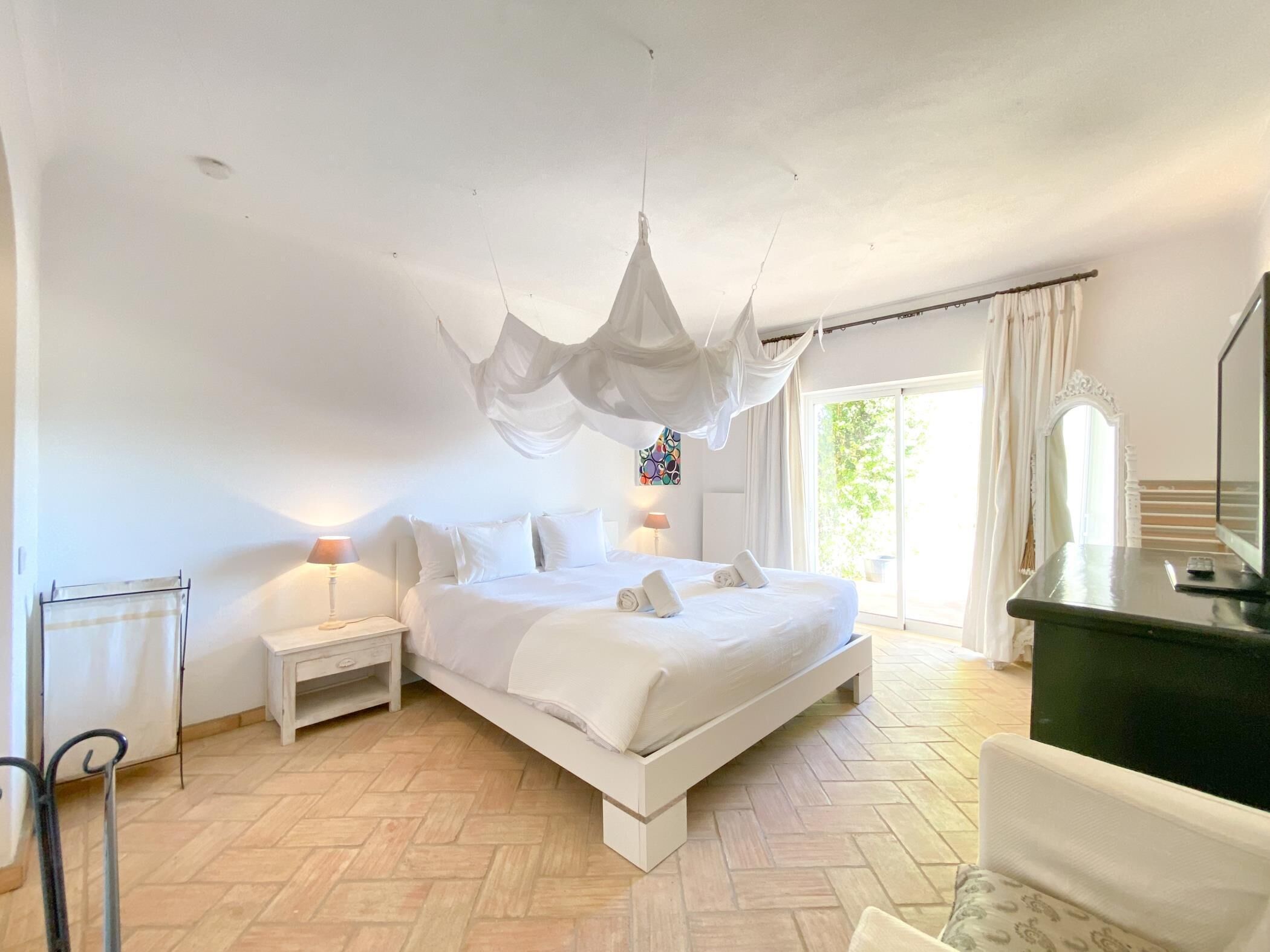 A bedroom with a bed, bedside tables, a chair, a desk, and a large window.