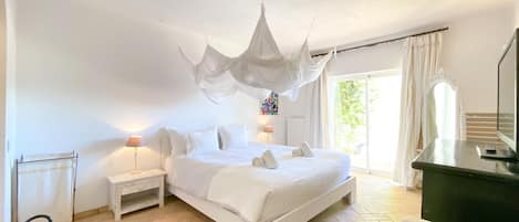 A bedroom with a bed, bedside tables, a chair, a desk, and a large window.