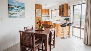 Een moderne keuken met houten kasten, een eettafel met stoelen en een groot raam met gordijnen.