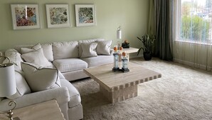 Een woonkamer met een hoekbank, een houten salontafel en drie ingelijste abstracte schilderijen aan de muur.