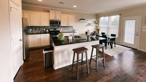 A modern kitchen with white cabinets, a stainless steel refrigerator, a microwave, and a large island with stools. - Spacious, New build 4 bedroom house in Conroe (Conroe)