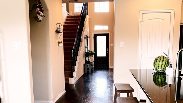 A spacious hallway with a wooden floor, a staircase, and a kitchen area with a bar counter and stools. - Spacious, New build 4 bedroom house in Conroe (Conroe)