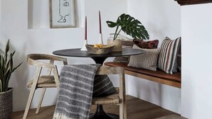 A dining area with a wooden table, a hanging pendant light, a potted plant, and a framed picture on the wall.