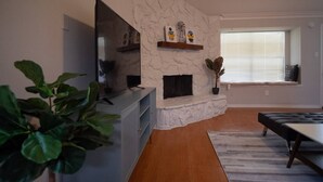 A living room with a stone fireplace, a flat-screen TV, a dining area with a table and chairs, and a large plant. - Cozy and Spacious 3 Bedroom Home in Sugarland (Sugar Land)