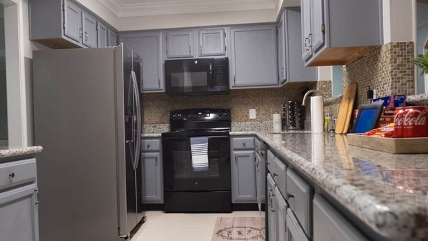 A kitchen with grey cabinets, a stainless steel refrigerator, a microwave, and a stove. - Cozy and Spacious 3 Bedroom Home in Sugarland (Sugar Land)
