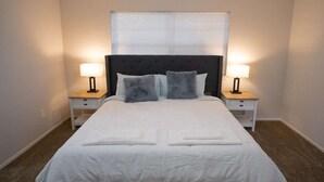 A neatly made bed with white bedding and two pillows, flanked by two bedside tables with lamps, in a room with beige walls and a ceiling fan. - Cozy and Spacious 3 Bedroom Home in Sugarland (Sugar Land)