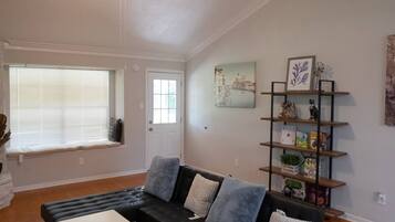A living room with a black sectional sofa, a white coffee table, a ceiling fan, a bookshelf, and a window with blinds.