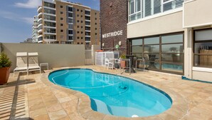 A swimming pool area with lounge chairs, a brick building labeled "WESTRIDGE", and a view of other residential buildings. - First floor apartment with beautiful sea view (Cape Town)