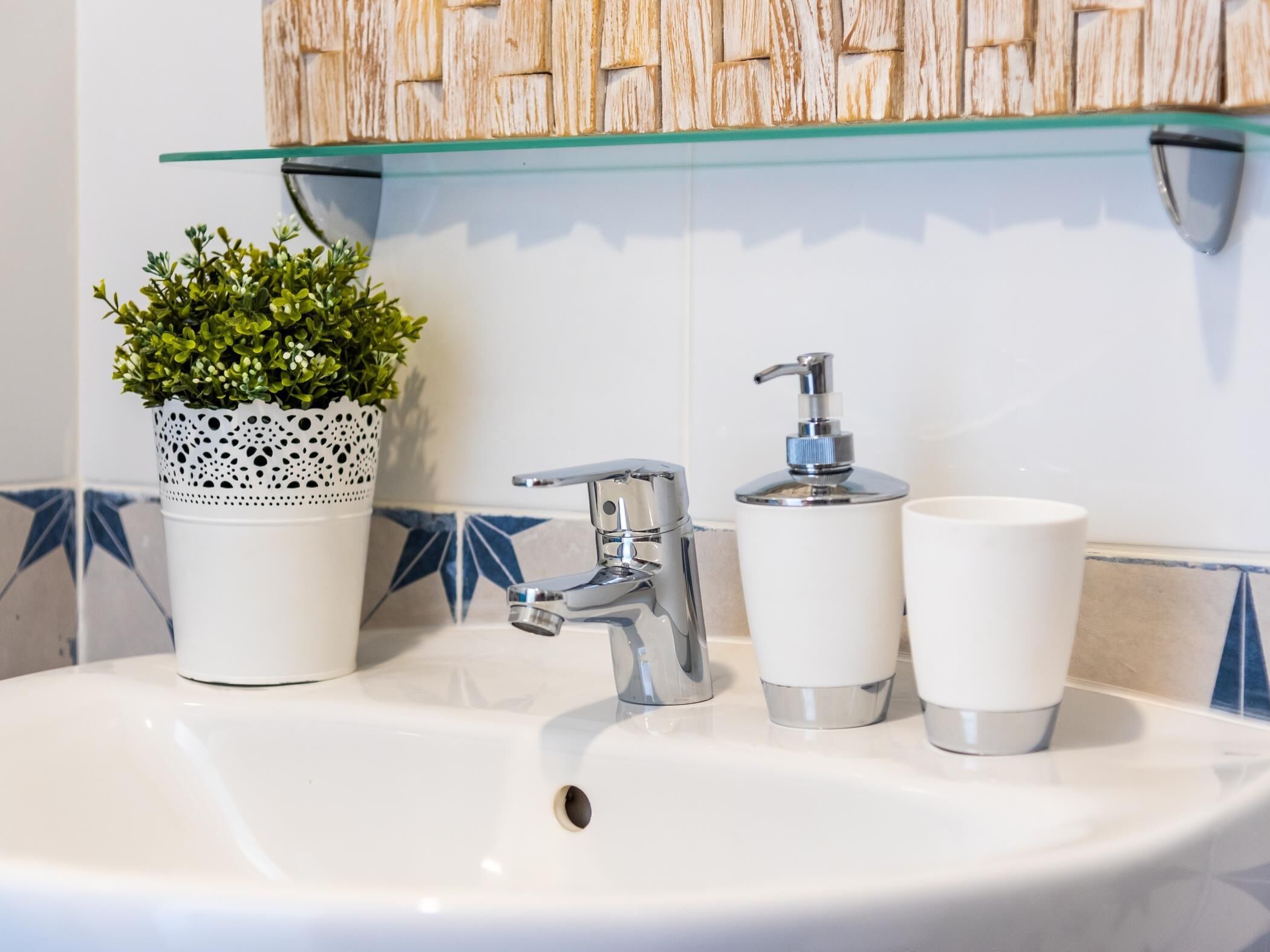 Un lavamanos de baño con una llave moderna, una planta en maceta y dos tazas blancas.
