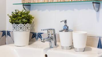 Un lavamanos de baño con una llave moderna, una planta en maceta y dos tazas blancas.
