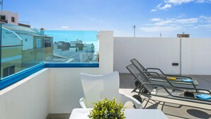 A rooftop terrace with a clear view of the city, a white wall, and a table with two chairs.