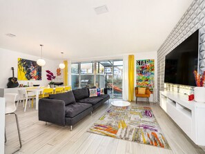 A modern living room with a sofa, dining table, and chairs, a TV, and a large window.