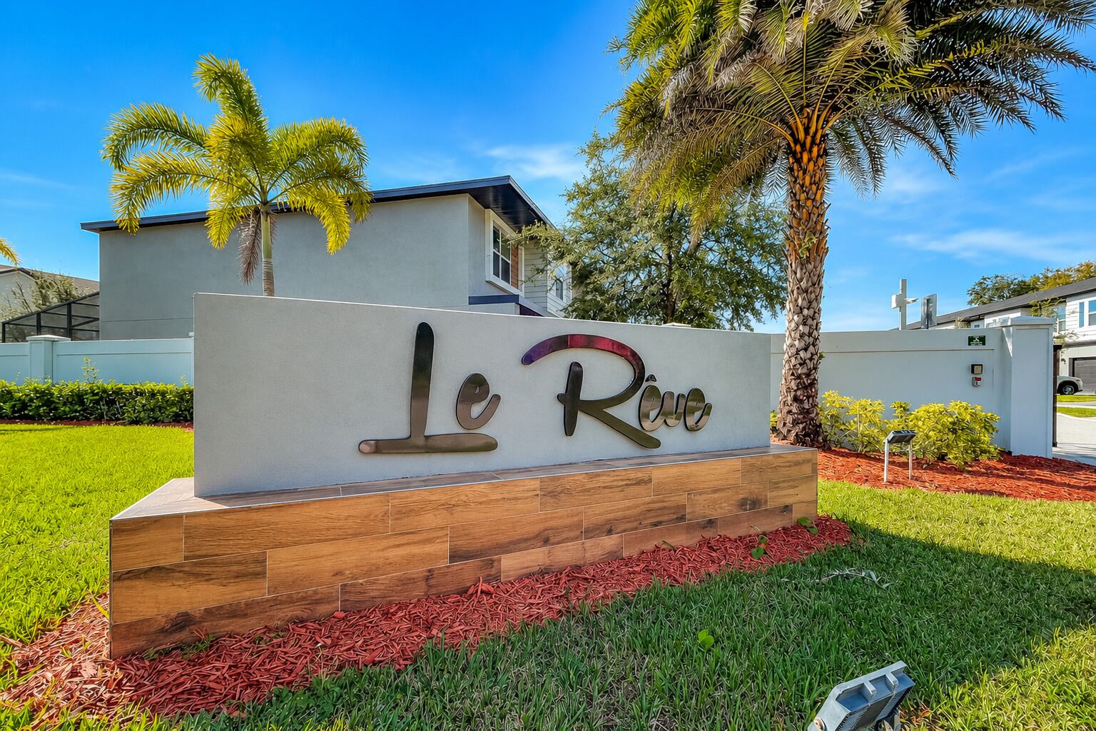 A sign with 'Le Rio' written in stylized letters, surrounded by a landscaped area with grass and palm trees.