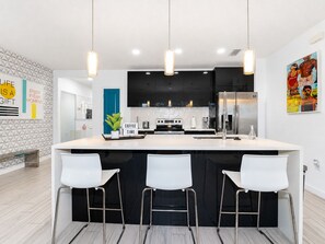 Una cocina moderna con una isla central, taburetes de bar, iluminación colgante y una zona de café.