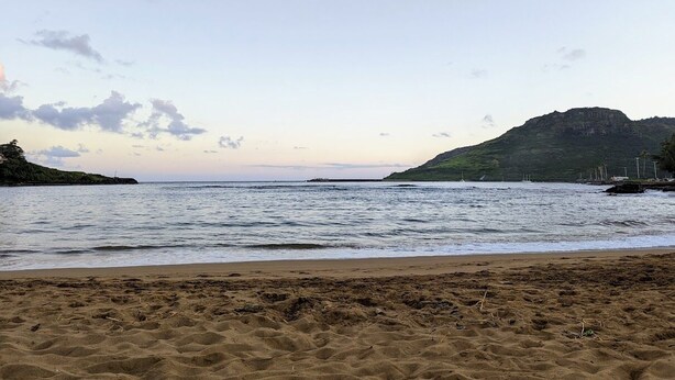 Ein Strand mit sandigem Ufer, ruhigem Meer und einem fernen Berg.