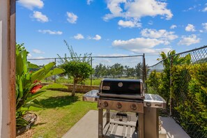 A barbecue grill in a backyard with a chain-link fence, potted plants, and a clear blue sky. - Walk to Kalapaki Beach, 3 lanais, full AC (Lihue)