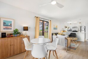A modern hotel room with a dining area, a kitchen, and a balcony with curtains.