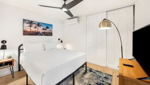 Ein Schlafzimmer mit Bett, Schreibtisch, Stuhl, Stehlampe, Deckenventilator und einer Tür.