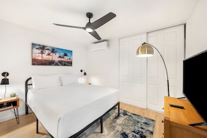 A bedroom with a bed, a desk, a chair, a standing lamp, a ceiling fan, and a door. - Walk to Kalapaki Beach, 3 lanais, full AC (Lihue)