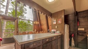A kitchen with a large island, wooden cabinets, and a refrigerator. There are framed pictures on the wall and a window with a view of trees. - Lazy Dog Lodge - hot tub, dog friendly, wifi (Ruidoso)
