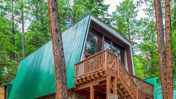A cabin with a wooden deck and stairs leading to a windowed porch. - Lazy Dog Lodge - hot tub, dog friendly, wifi (Ruidoso)
