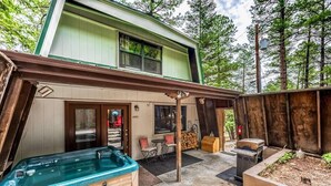 A two-story house with a covered patio area featuring a hot tub, outdoor seating, and a barbecue grill. - Lazy Dog Lodge - hot tub, dog friendly, wifi (Ruidoso)