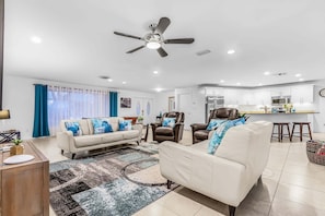 A modern living room with a sofa, armchairs, a coffee table, a rug, and a ceiling fan.