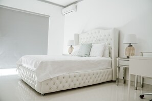 Quarto moderno com cabeceira estofada, uma janela grande e uma cômoda branca com duas luminárias.