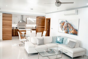 Uma sala de estar moderna com uma mesa de centro de vidro, sofá branco e uma área de jantar com cadeiras brancas.
