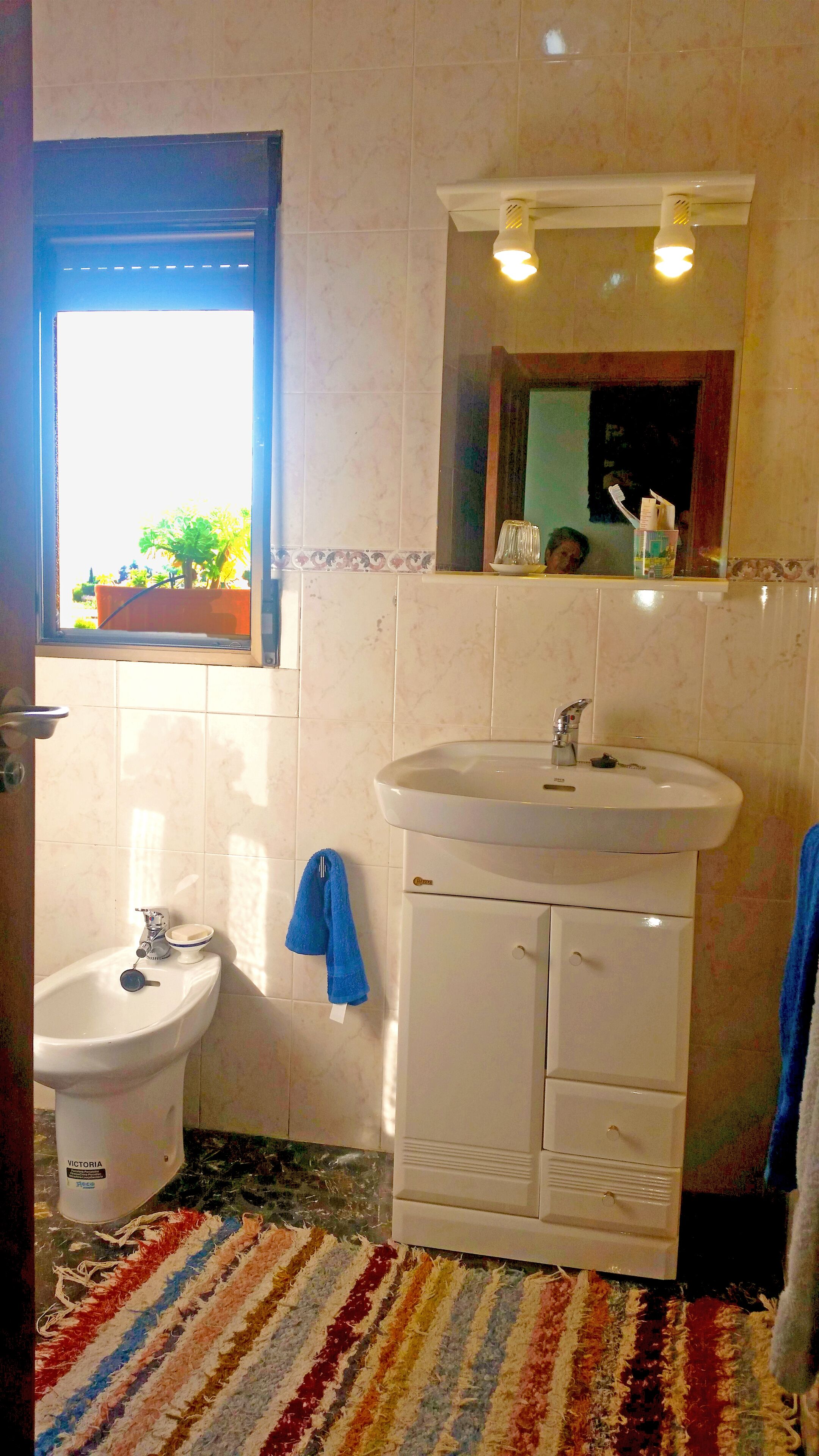 A bathroom with a bidet, a sink, and a mirror. There is a window with a view of greenery outside.