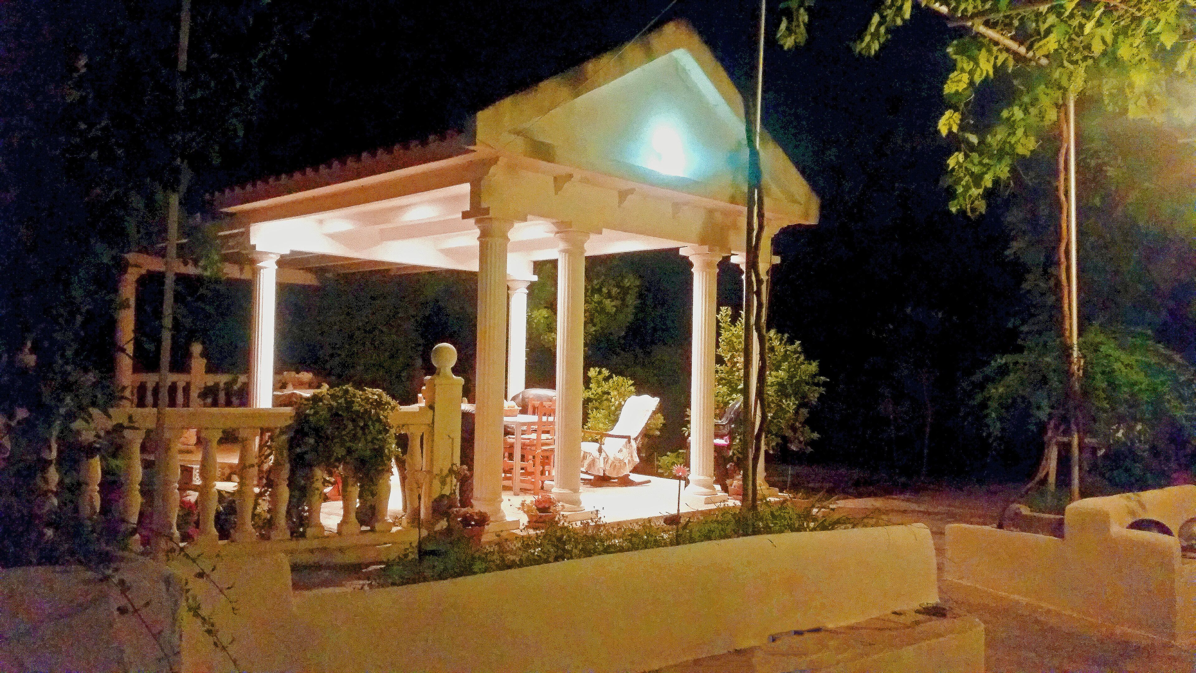 Un gazebo con tetto bianco e colonne, circondato da piante in vaso e mobili da giardino.