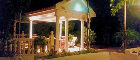 Un gazebo con tetto bianco e colonne, circondato da piante in vaso e mobili da giardino.