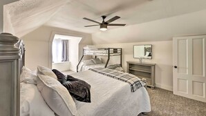 Een slaapkamer met een stapelbed, een plafondventilator, een raam met gordijnen, een nachtkastje met spiegel en een deur.