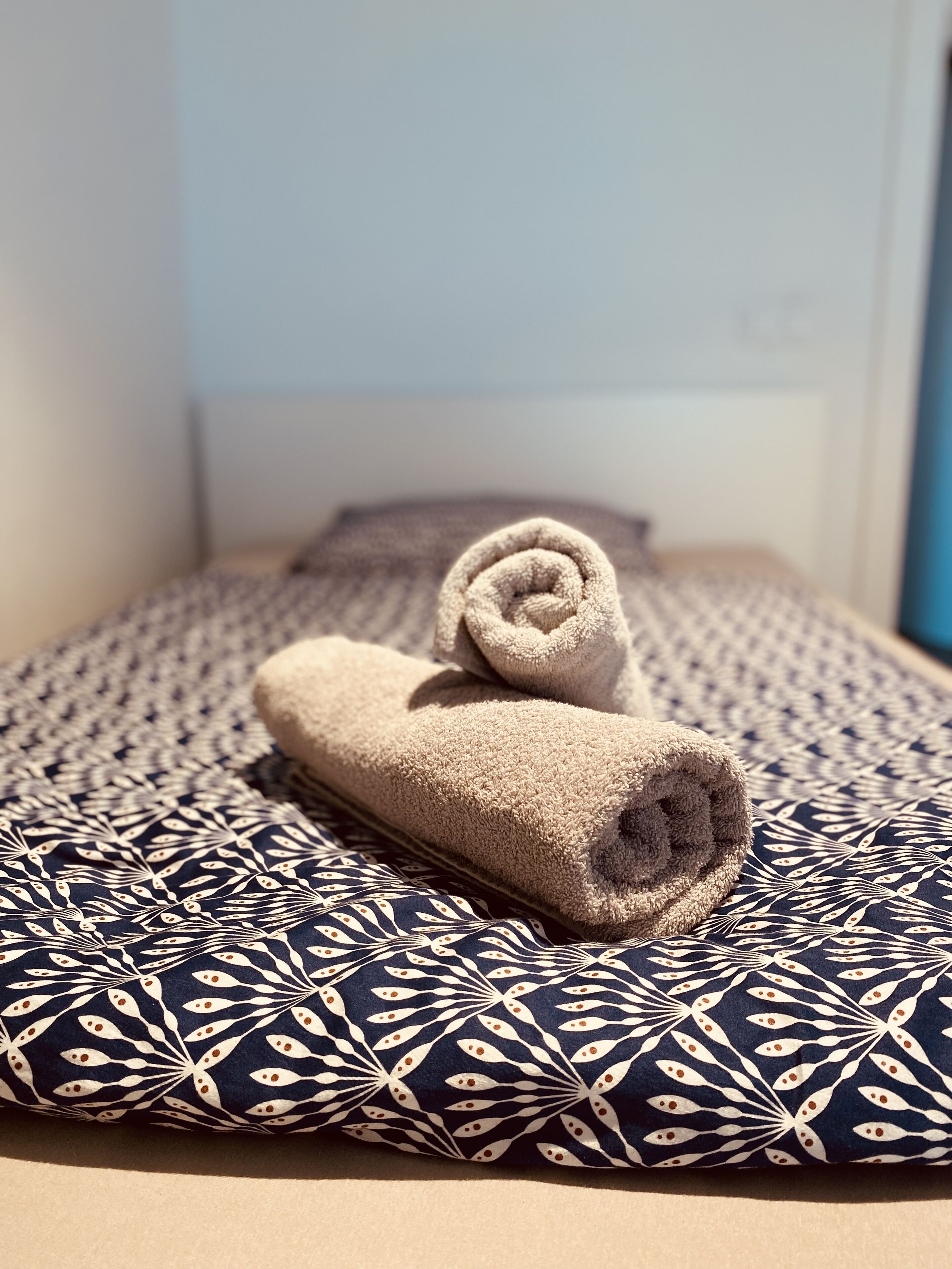 A bed with a rolled towel and a patterned pillow.