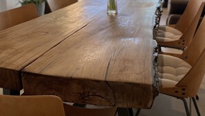 Une table à manger en bois, ornée d’un vase de tulipes, entourée de chaises, dans une pièce moderne dotée d’une grande fenêtre donnant sur l’extérieur.