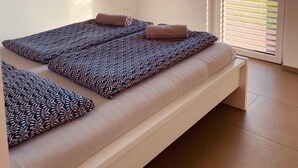 Une chambre à coucher moderne avec un lit, une œuvre d’art bleue accrochée au mur et une fenêtre avec des stores.