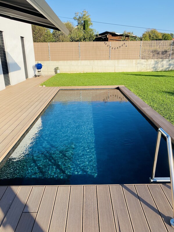 Une piscine rectangulaire à l’eau claire, entourée d’une terrasse en bois et d’une pelouse.