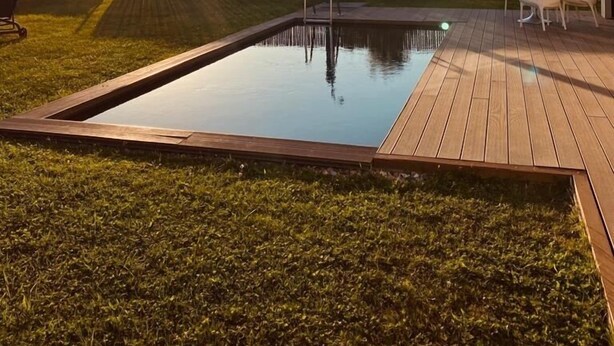 Une piscine dotée d’une terrasse en bois, entourée d’une pelouse et d’une clôture.