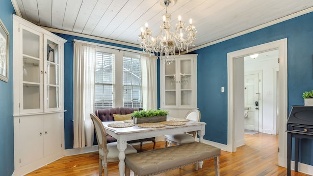 A dining area with a white table, bench, and chandelier, against a blue wall with wooden flooring. - Back on Market! Baton Rouge Cottage < 3 Mi to LSU (Baton Rouge)