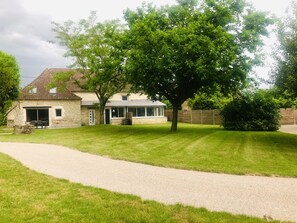 Une maison en pierre avec une allée pavée, une pelouse et un grand arbre devant.