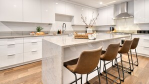 A modern kitchen with white cabinetry, a marble island, and three bar stools.