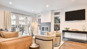 A modern living room with a sofa, armchairs, a TV, and a fireplace.