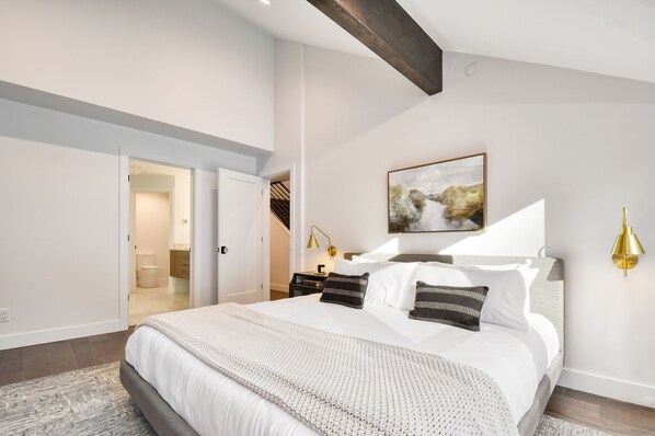 Un dormitorio moderno con una cama grande, una mesita de noche, una lámpara de pared y un cuadro.