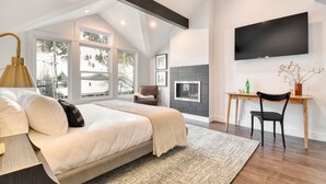 A modern bedroom with a large bed, a desk, and a fireplace.