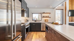 A modern kitchen with stainless steel appliances, wooden cabinets, and a large window providing natural light.