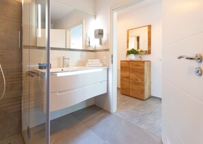 A modern bathroom with a glass shower enclosure, a white vanity with a mirror, and a wooden cabinet. - Domizil Meerzeit, App. 2 (Heringsdorf)