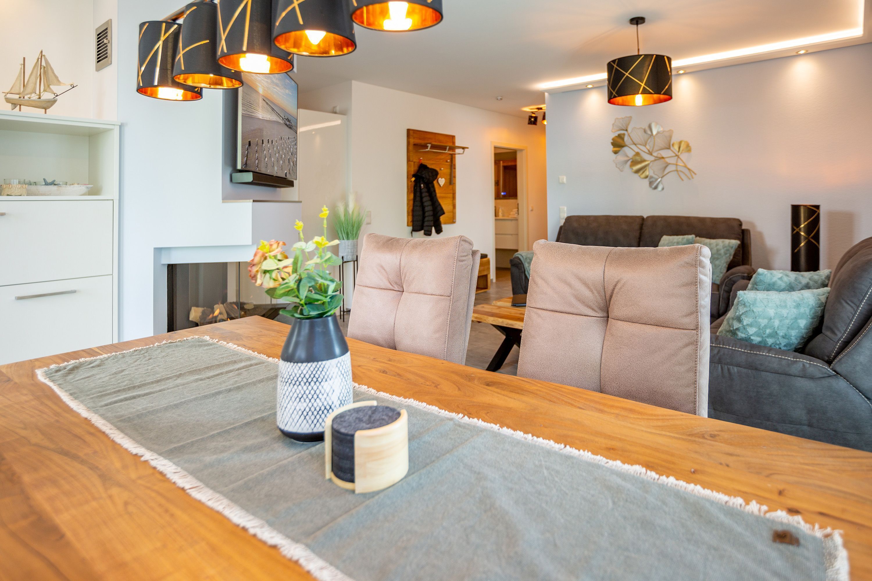 Een moderne woonkamer met een houten eettafel, comfortabele stoelen, een open haard en moderne verlichtingsarmaturen.